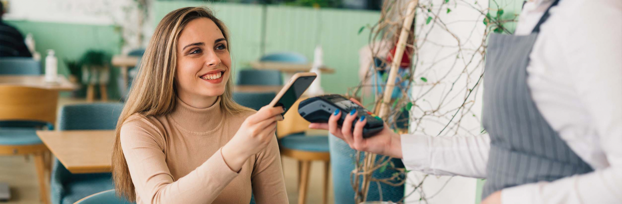 Woman sitting in coffee shop paying with her cell phone