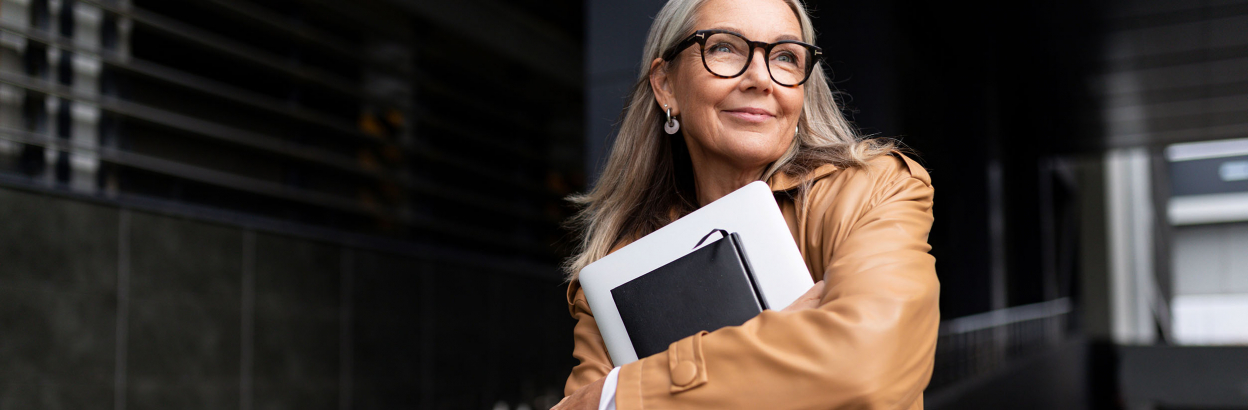 Smiling business woman outside holding laptop and notebook