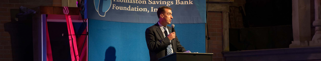 Stephen Lewis speaking on a podium in front of a Thomaston Savings Bank Foundation, Inc. backdrop.