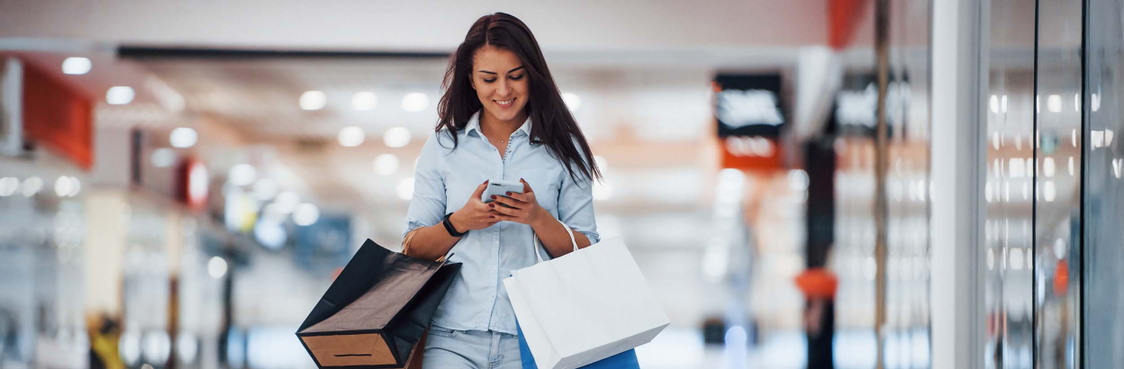 A woman looking at her cell phone while shopping and holding bags