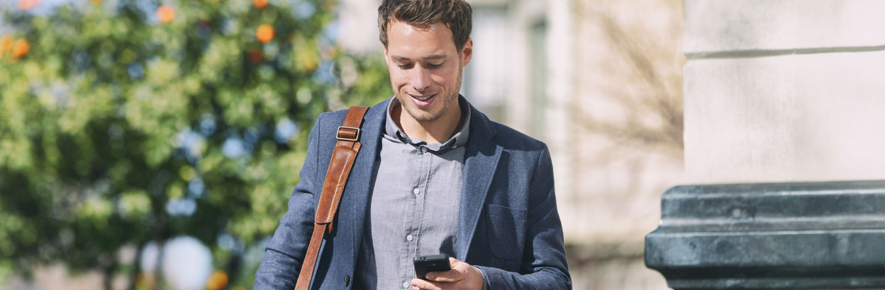 Businessman using phone while walking in a city with trees in background