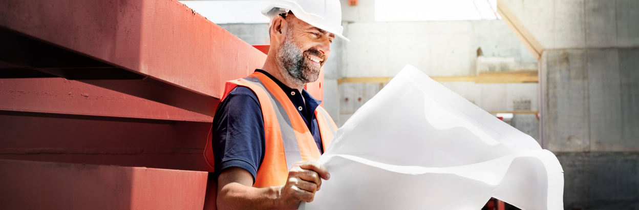 A smiling man wearing a hard hat and vest looking at a site planning concept