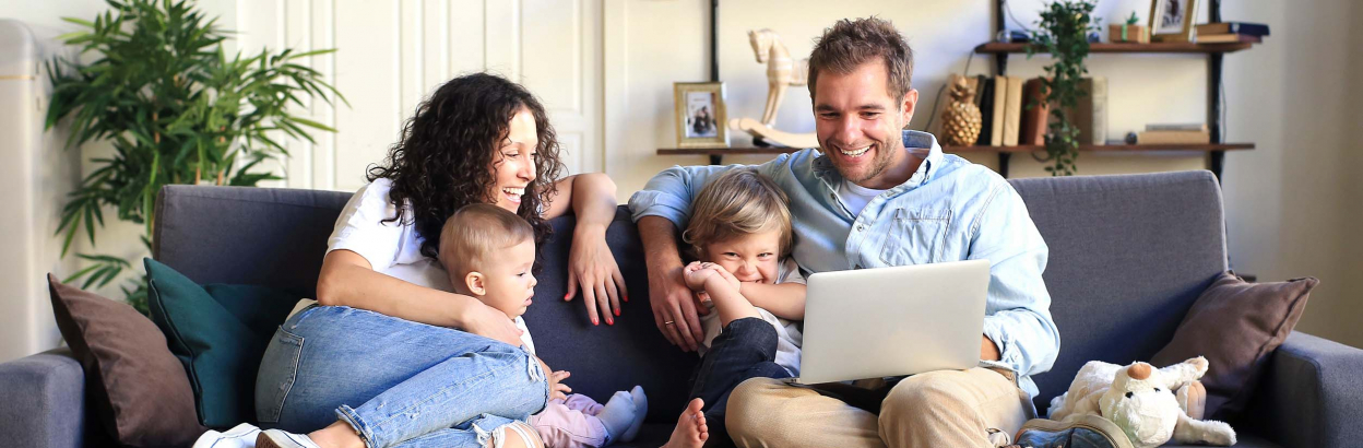 Parents and their two children sitting together on a couch while the father uses his laptop