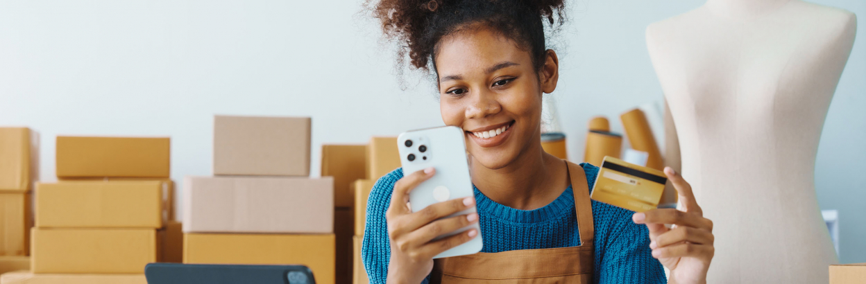 Businesswoman using credit card and phone in her shop with packages in background