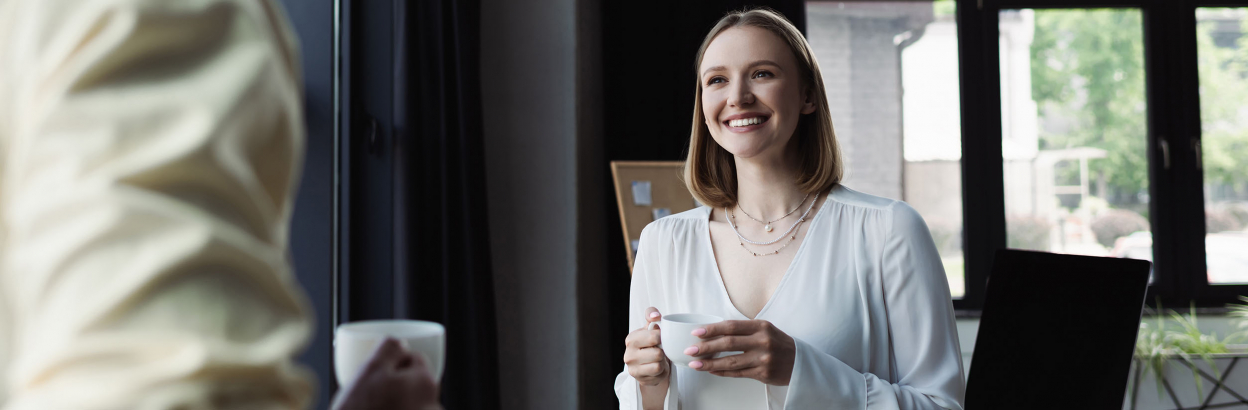Smiling businesswoman with cup of coffee speaking with colleague in an office
