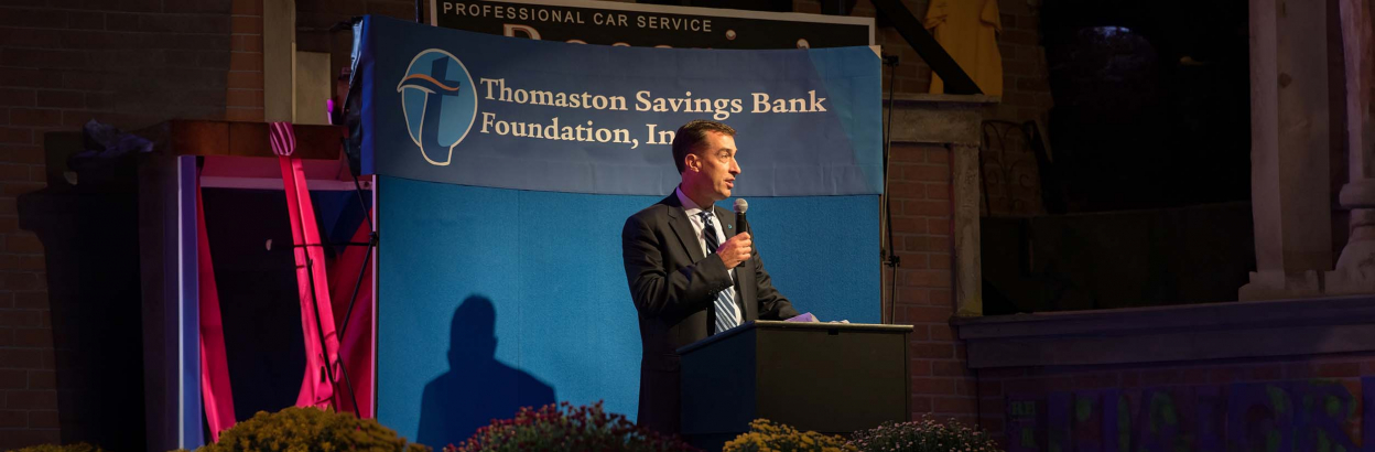 Stephen Lewis speaking on a podium in front of a Thomaston Savings Bank Foundation, Inc. backdrop.