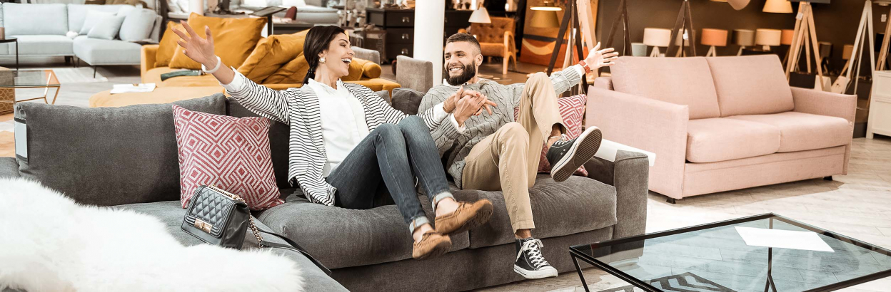 A couple holding hands and laughing while sitting on a couch in a furniture store