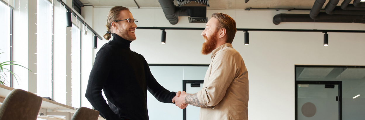 Side view of entrepreneur in casual clothes shaking hands with bearded and tattooed business partner