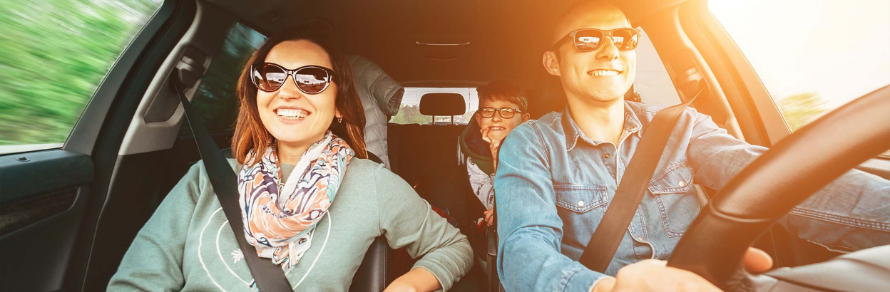 A smiling mother and father driving in car with child in backseat