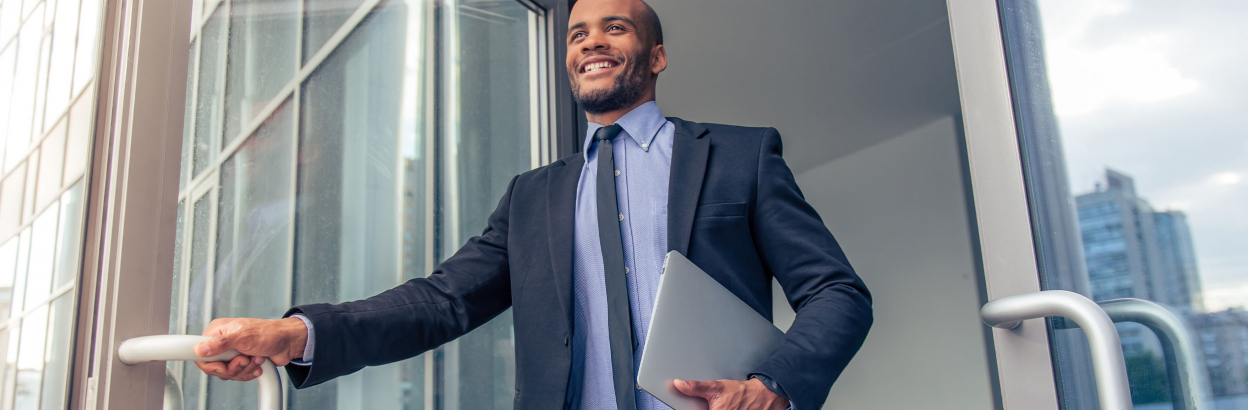 Man wearing a suit and holding a laptop and opening a glass door
