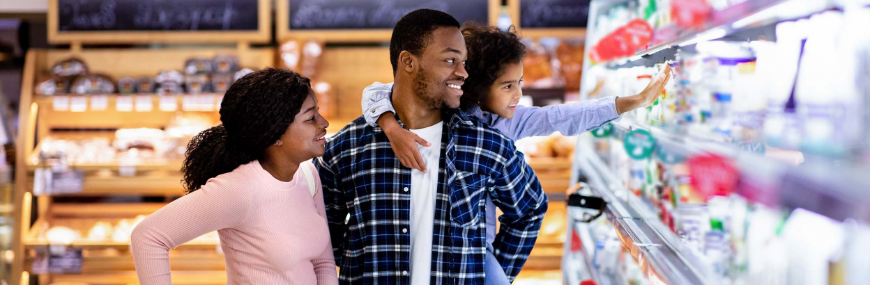 A couple with their child grocery shopping together in store, while child reaches towards an item