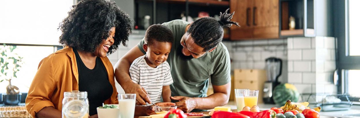 A couple teaching their young child how to cook in the kitchen, smiling and laughing