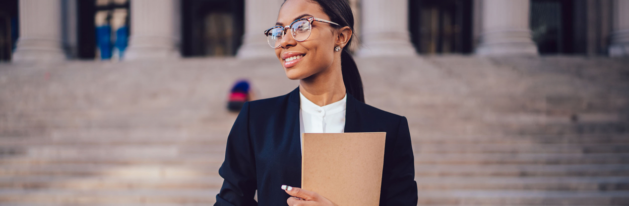 Successful female lawyer standing outdoors against courthouse building with folder in hands